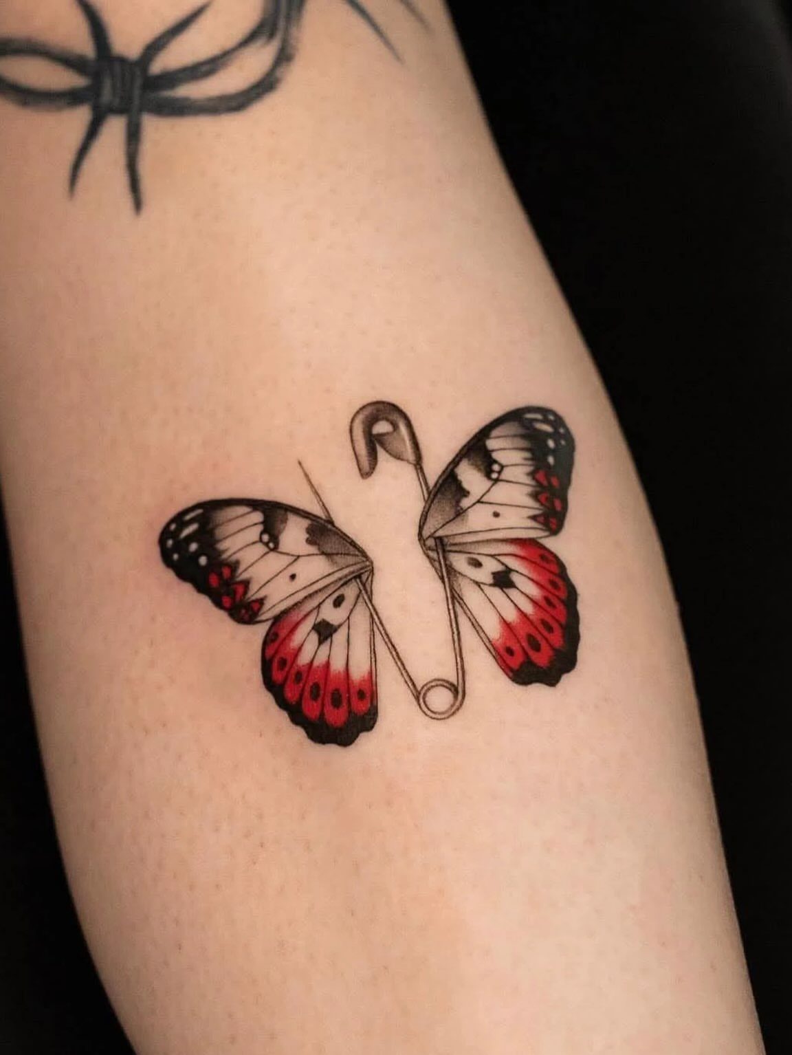 Butterfly tattoo with white and red wings and a safety pin body on skin.