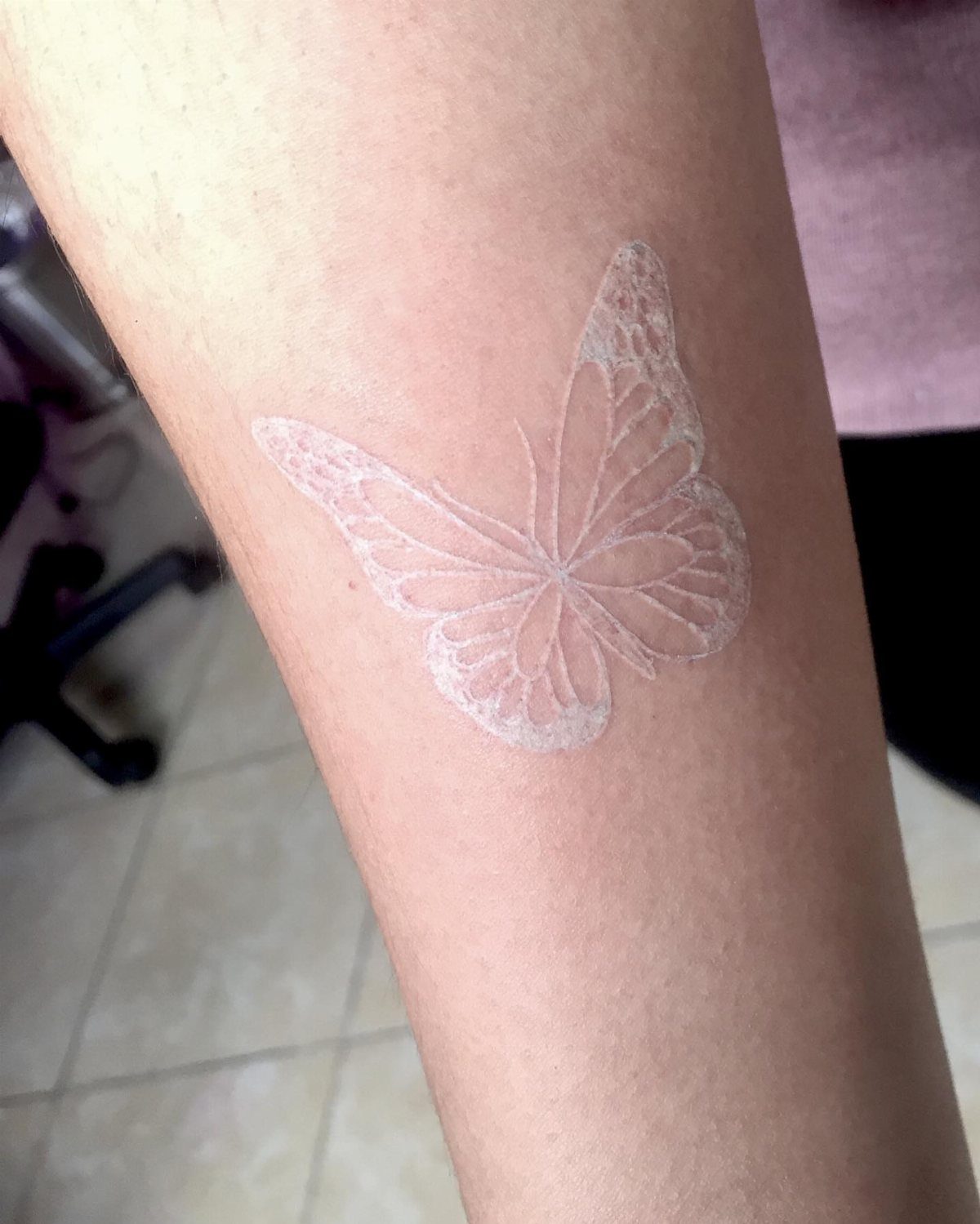 White ink butterfly tattoo on a person's forearm with detailed wing patterns