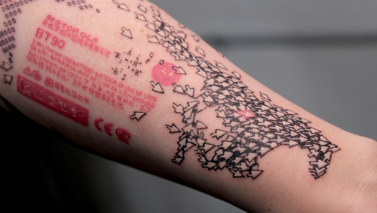 Tattoos on an arm featuring red technical text and many black computer cursor arrows.