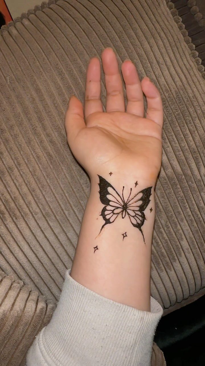 Butterfly tattoo with small stars on a person's inner wrist over brown fabric