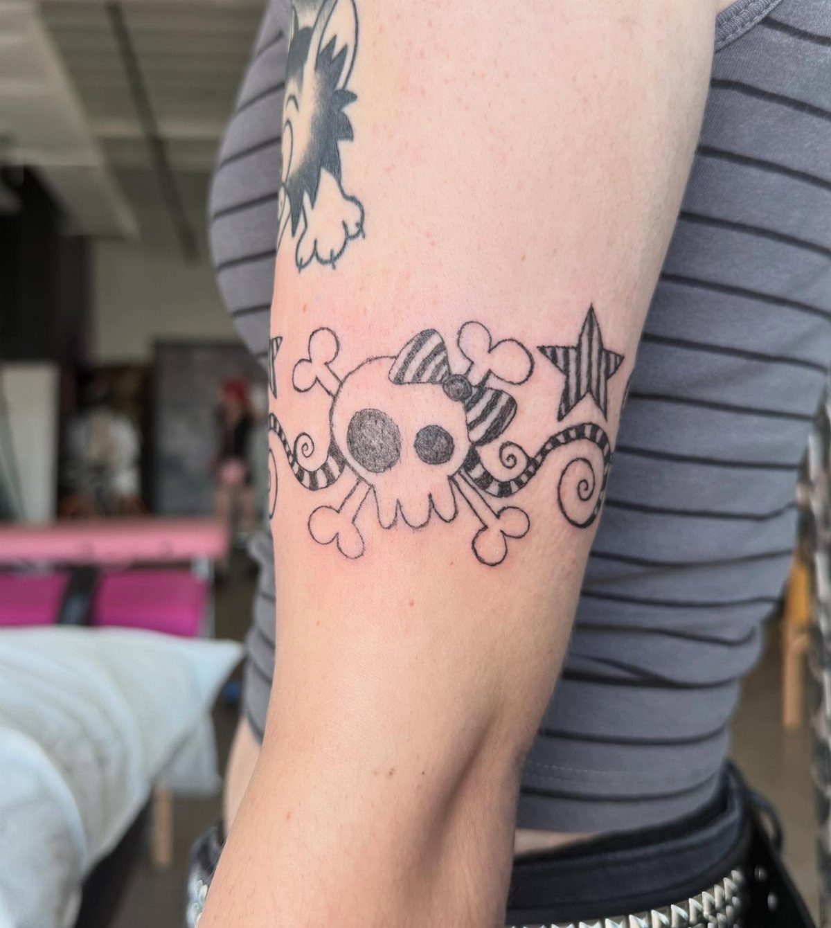 Skull and star tattoo on a person's upper arm wearing a striped shirt.