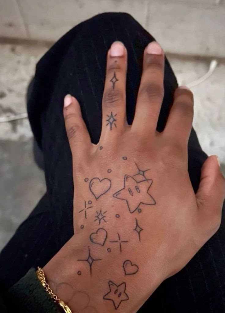 Hand with small black ink tattoos of stars, hearts, and sparkles.
