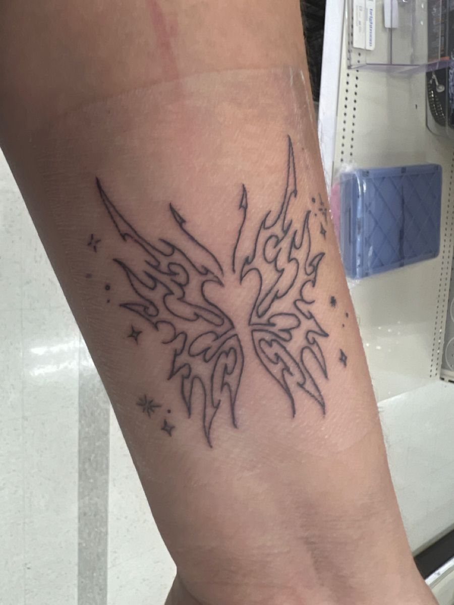 Tribal wing tattoo with small stars on a person's forearm