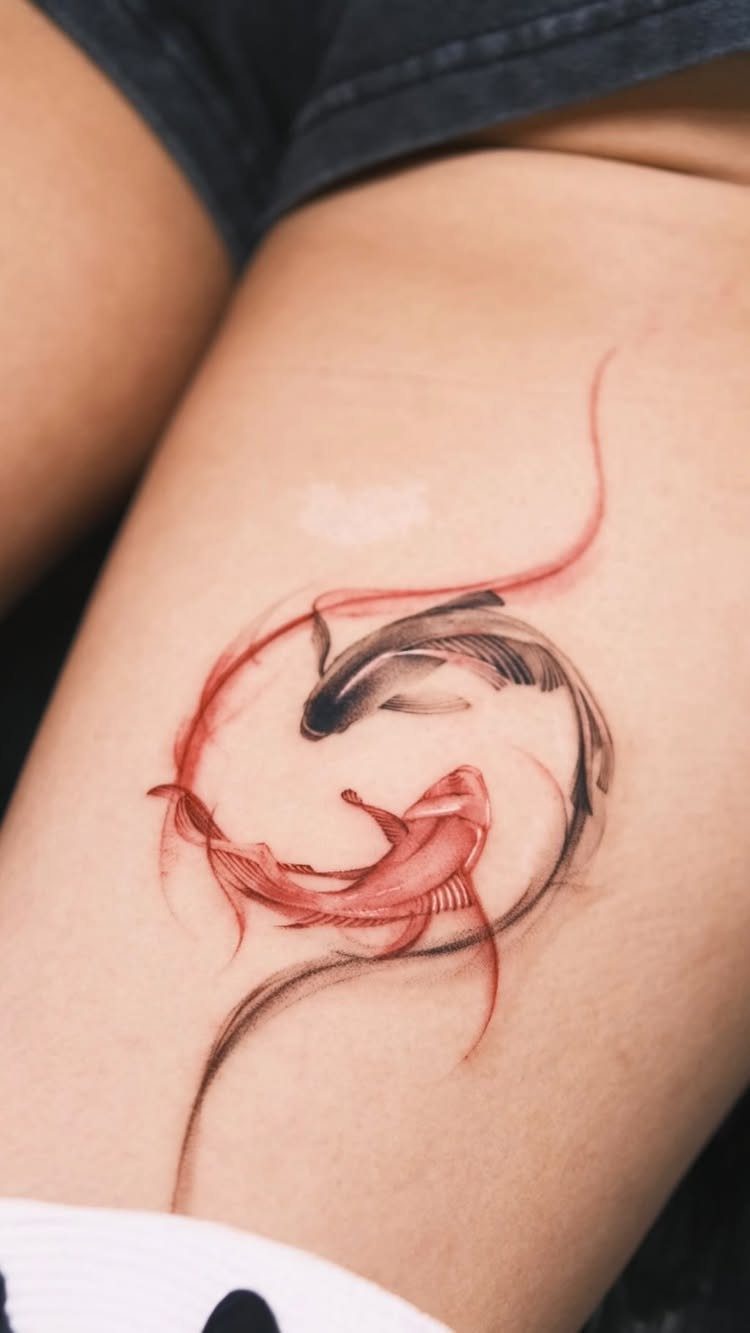 Two koi fish in a yin yang tattoo on a person's thigh.