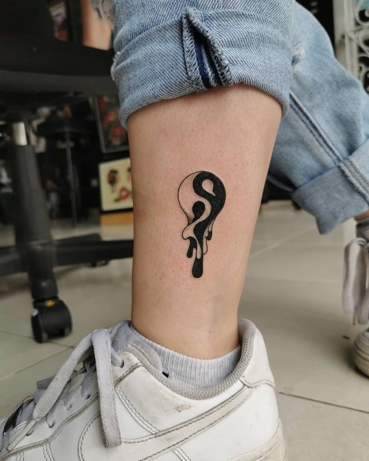 Melting yin yang tattoo on a person's ankle wearing white sneakers and blue jeans.