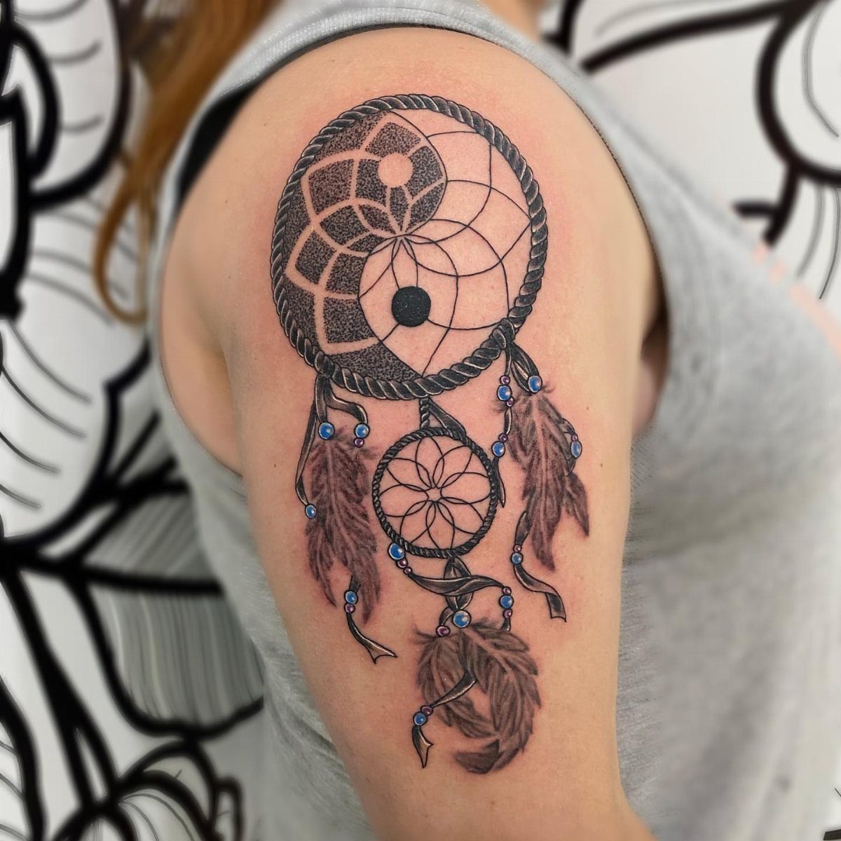 Yin yang dreamcatcher tattoo on an upper arm with feathers and blue beads.
