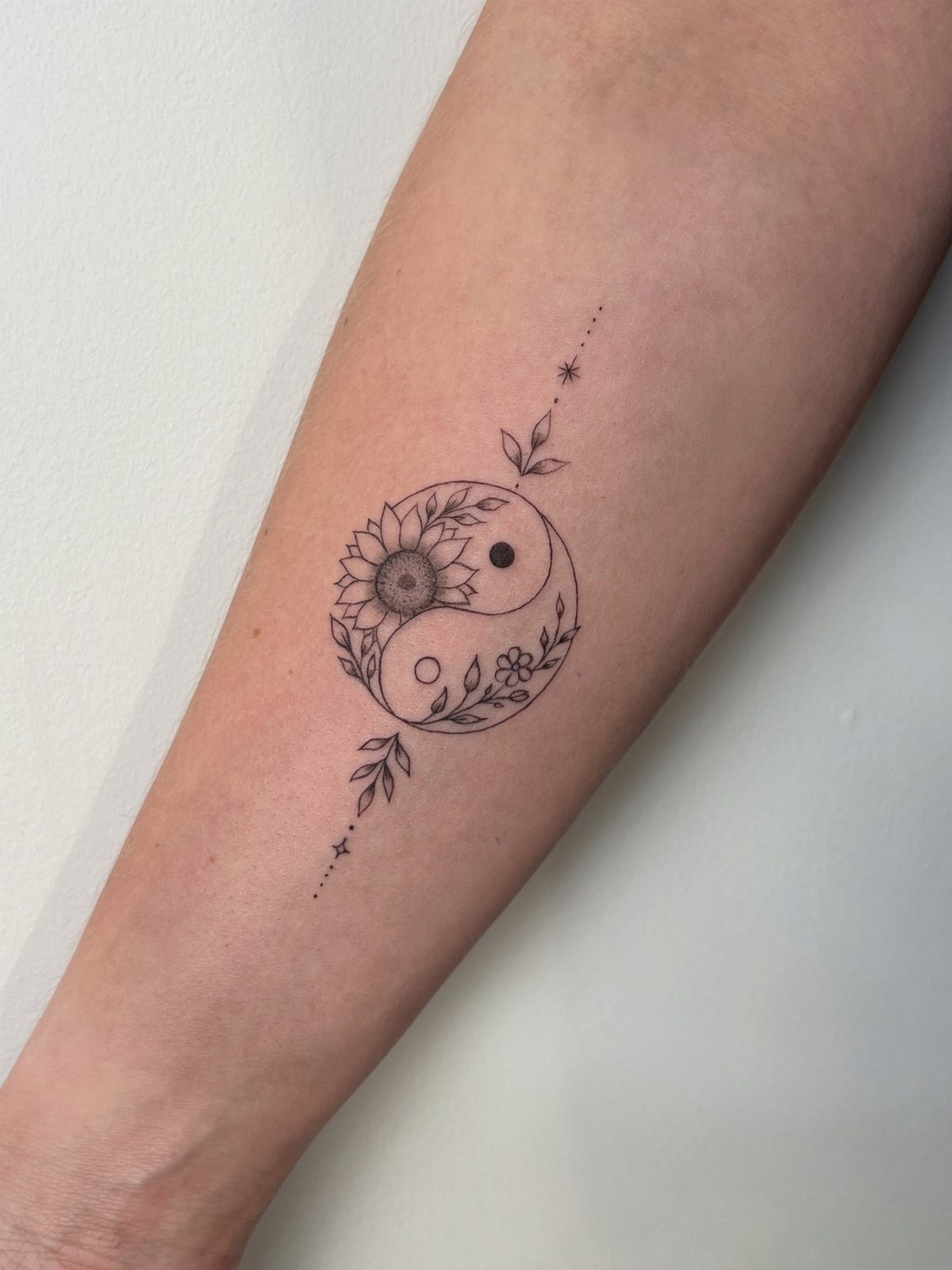 Yin yang tattoo on a forearm featuring a sunflower and floral vine elements.