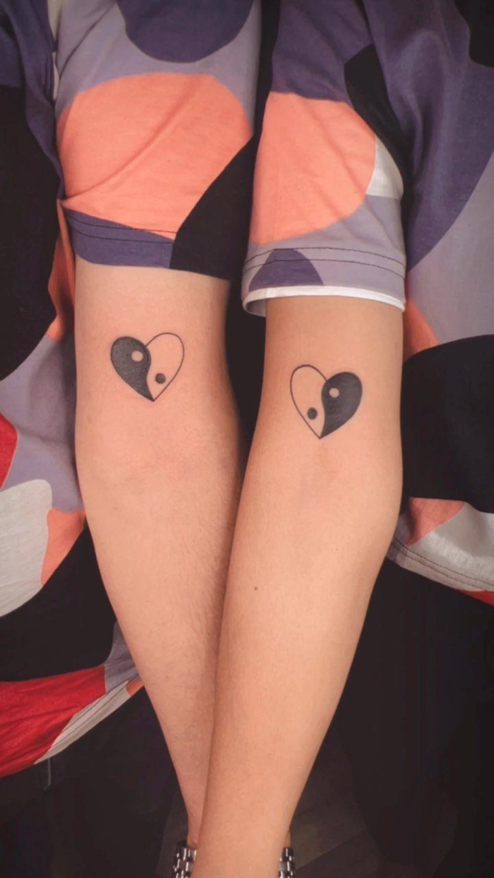 Heart-shaped yin yang tattoos on two forearms side-by-side.