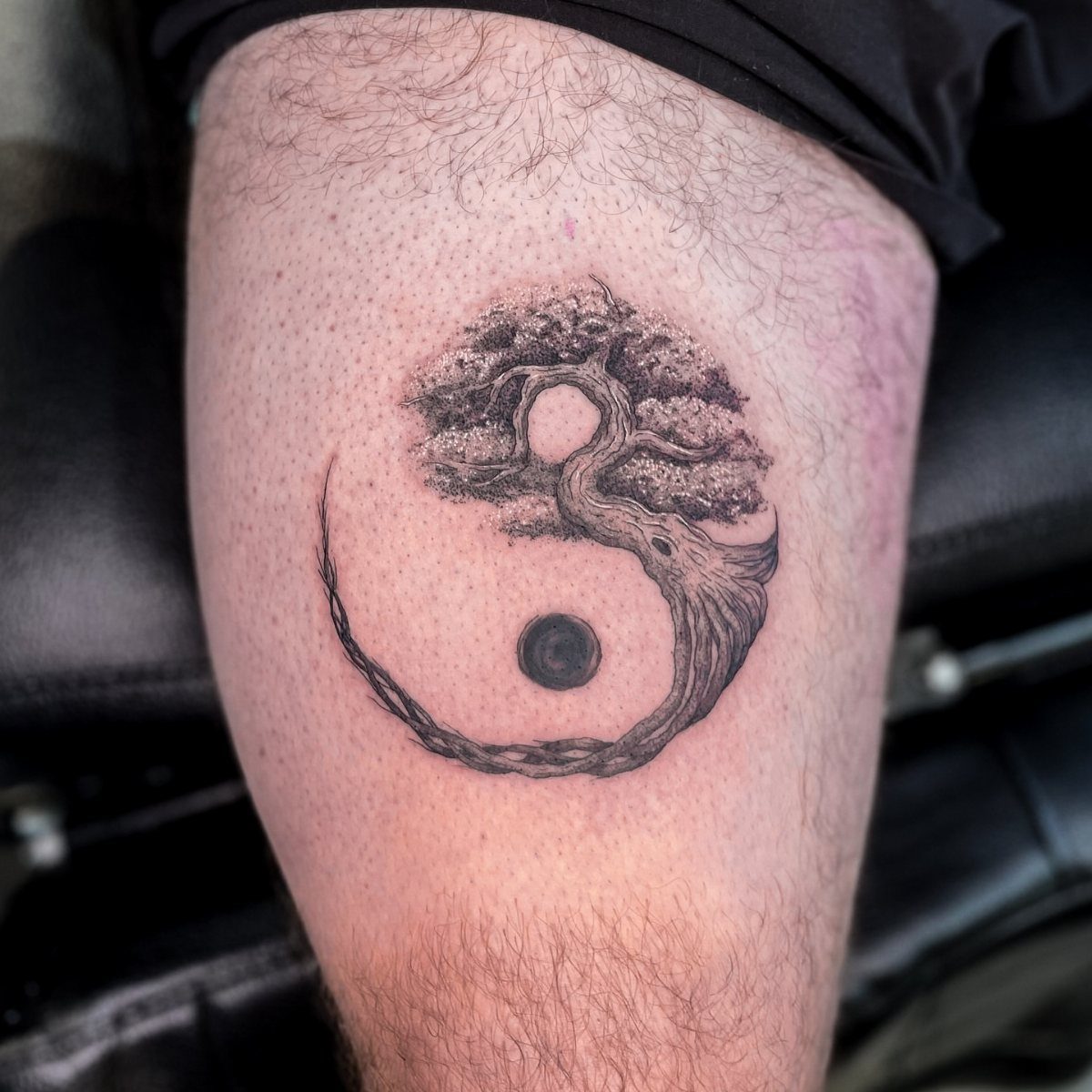 Yin yang tree of life tattoo on a person's leg in black ink.