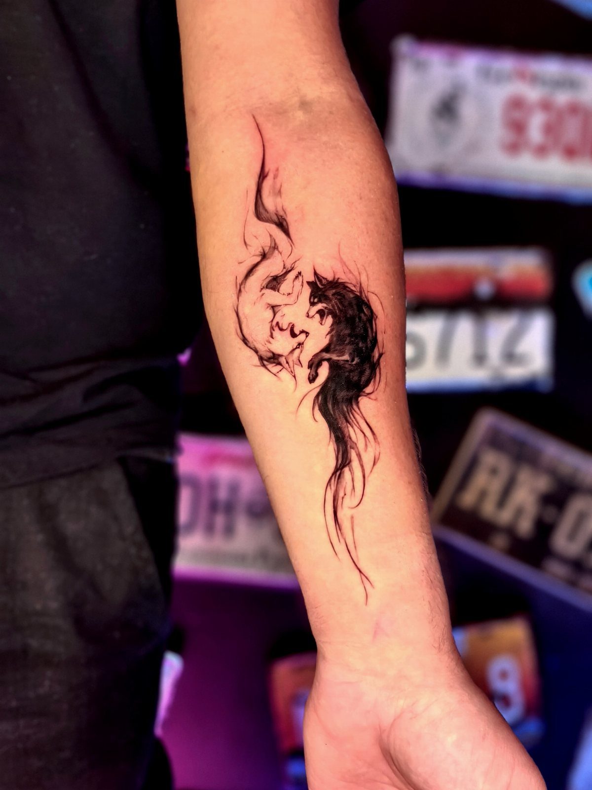 Yin yang wolf tattoo on a forearm with black and white stylized wolves.